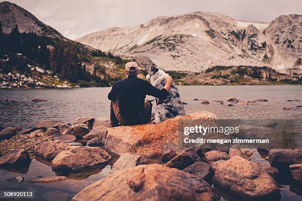 Man and dog sitting on rocks in water