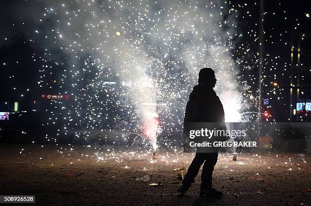 Man walks past fireworks in the street outside an apartment building in Beijing early on February 8, 2016 for the Lunar New Year celebrations which...