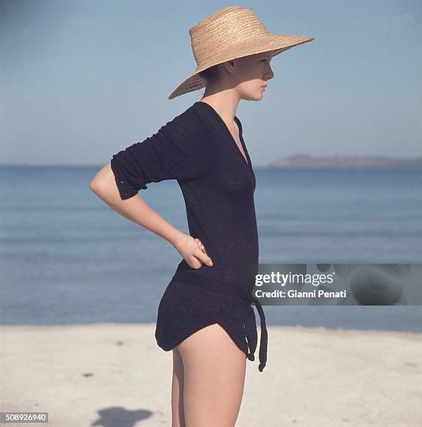 Model on beach wearing a V-neck black pullover with long cuffed sleeves, belt and shirttail bottom by Blairmoor Knitwear of Orlon and rayon.