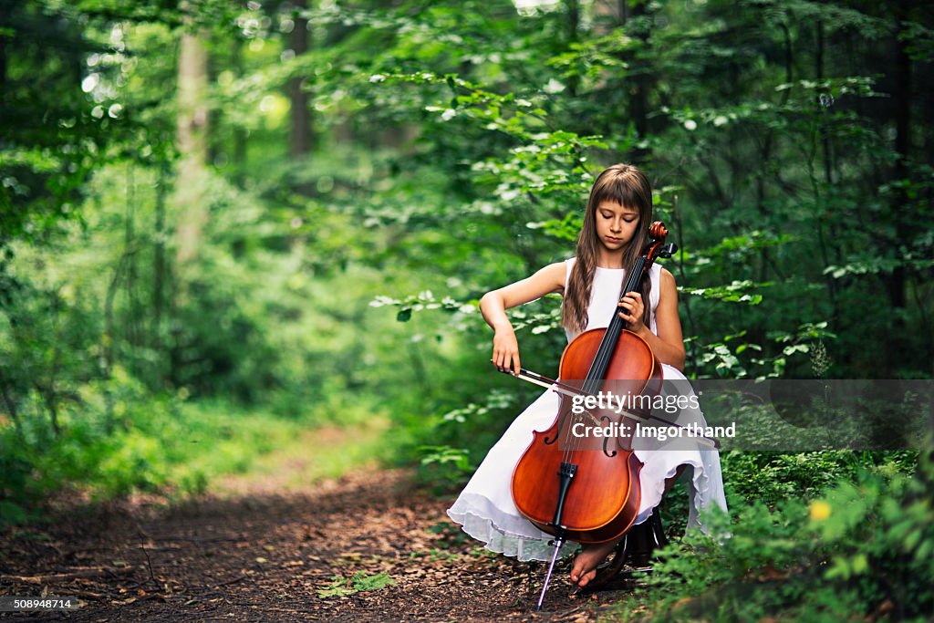 Music of nature - little cellist playing in beautiful forest