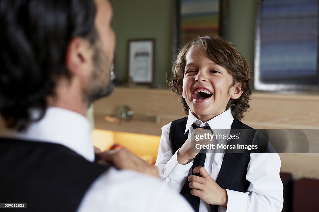 Boy adjusting tie while looking at father