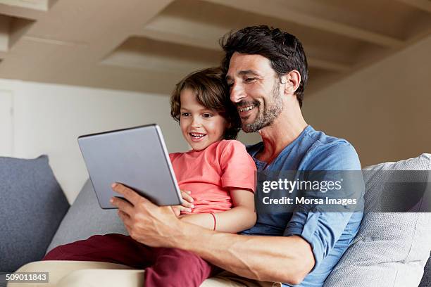 father and son using digital tablet on sofa - utilizar o tablet fotografías e imágenes de stock