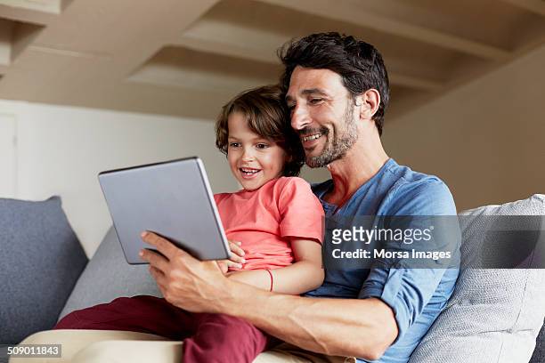father and son using digital tablet on sofa - family ipad stockfoto's en -beelden
