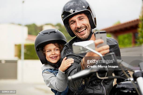 father and son taking self portrait on motorbike - motorcycle stock pictures, royalty-free photos & images