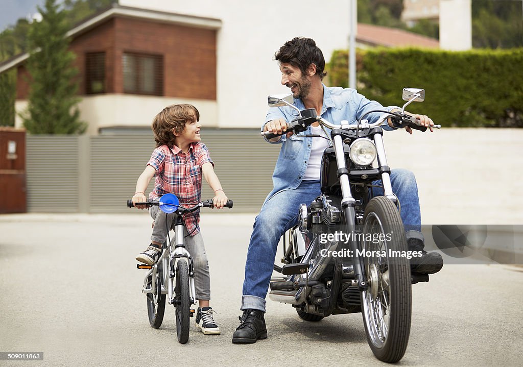 Man on motorbike looking at son riding bicycle