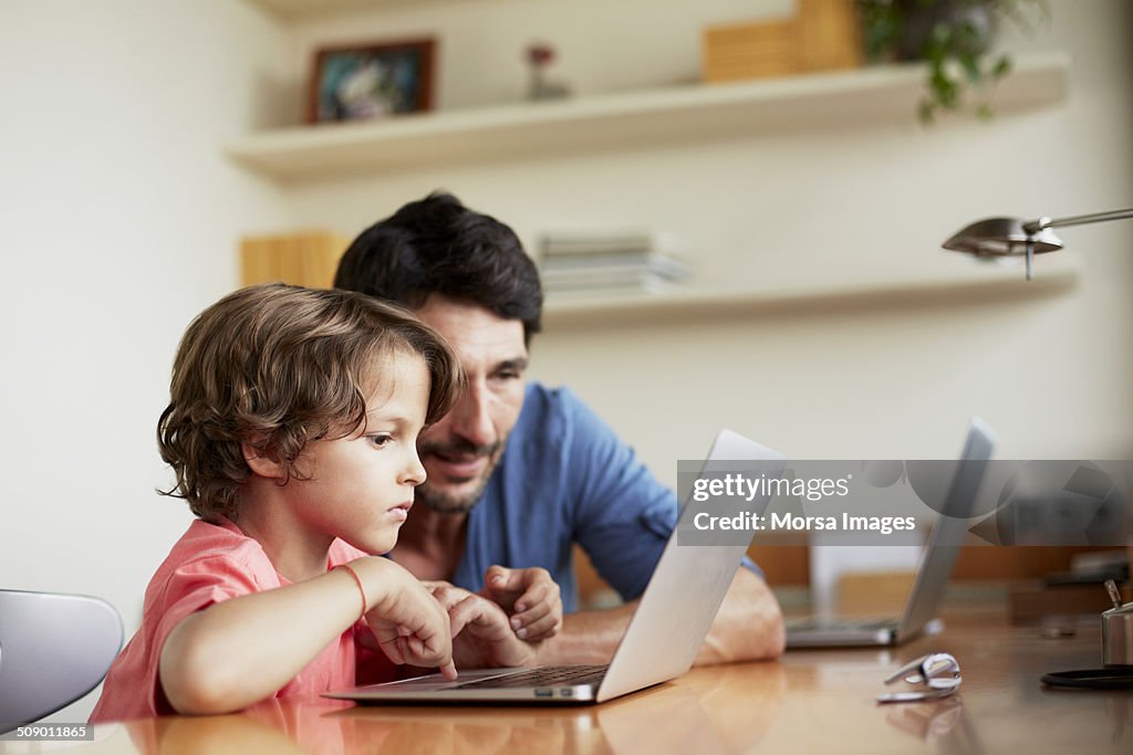 Man assisting son in using laptop