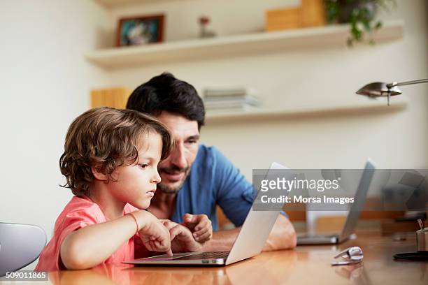 man assisting son in using laptop - family technology stock pictures, royalty-free photos & images
