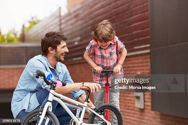 father looking at son pumping bicycle tire - luftpump bildbanksfoton och bilder