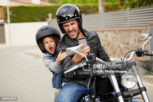 father and son taking self portrait on motorbike - moto humour photos et images de collection