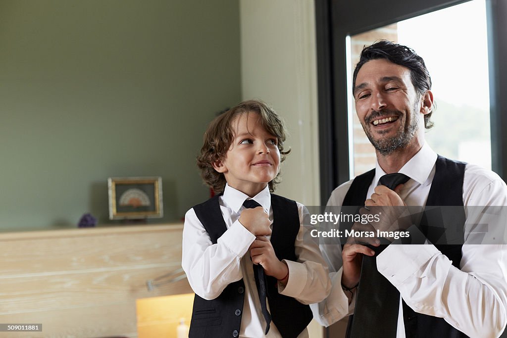 Boy adjusting tie while looking at father