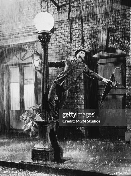 American actor and dancer Gene Kelly swings from a lamp post in a still from the film, 'Singin' In The Rain' directed by Kelly and Stanley Donen,...