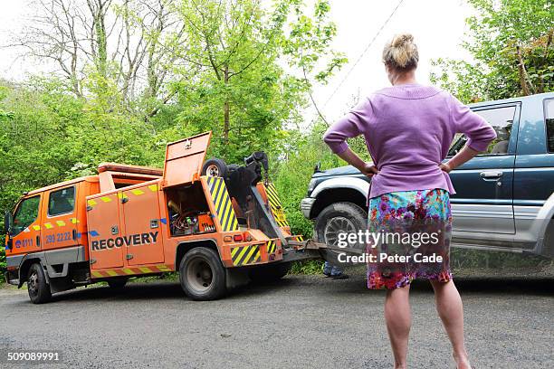 woman watching as broken down car is towed away - sleep stockfoto's en -beelden