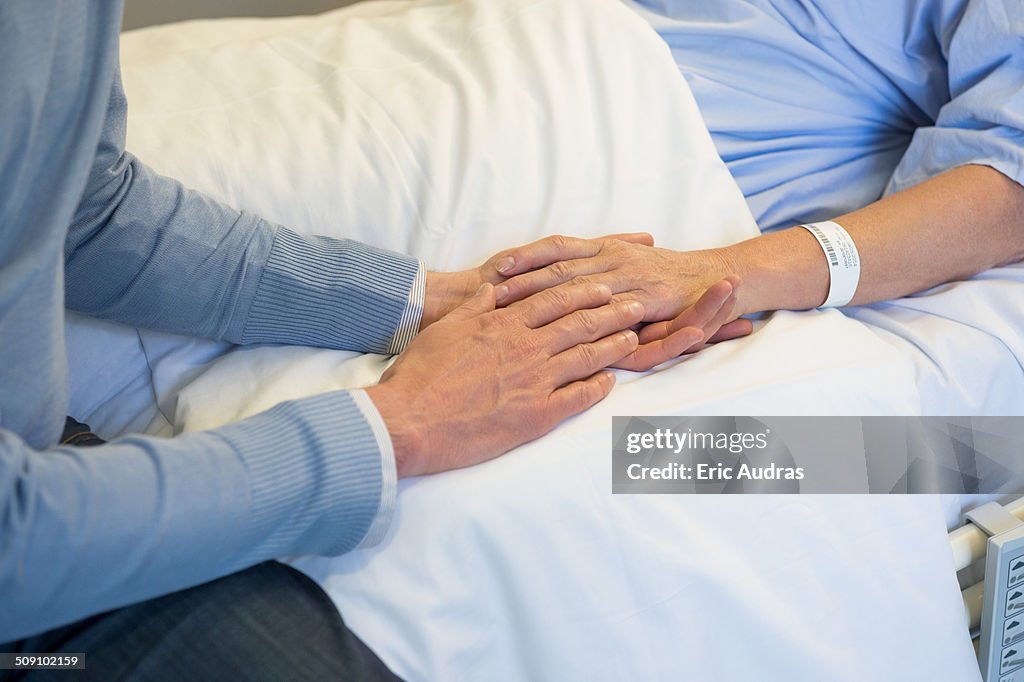 Man holding hands of his mother in hospital bed