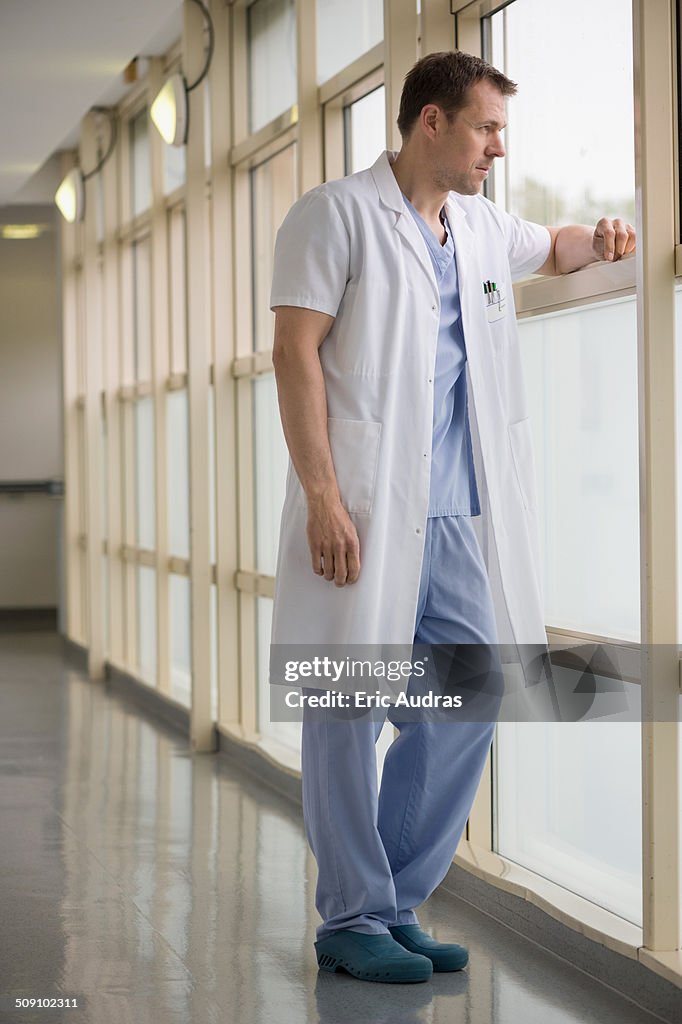 Male doctor standing in hospital looking out of window