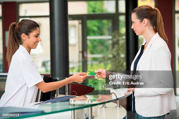 woman giving french social security card to receptionist at hospital reception desk - reception of france stock pictures, royalty-free photos & images