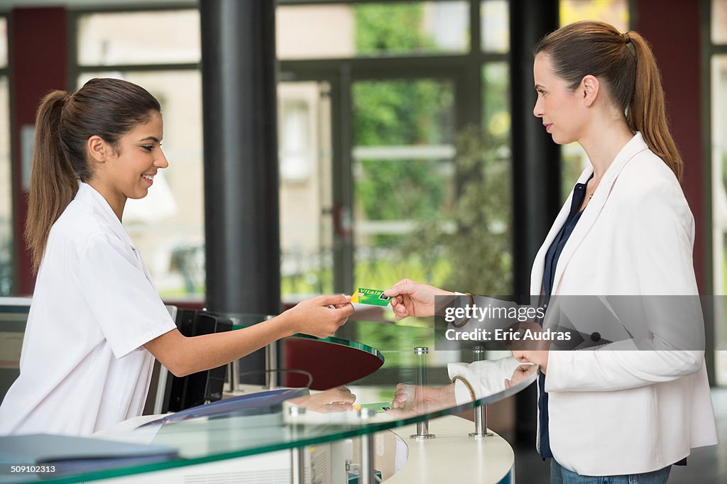 Woman giving french social security card to receptionist at hospital reception desk