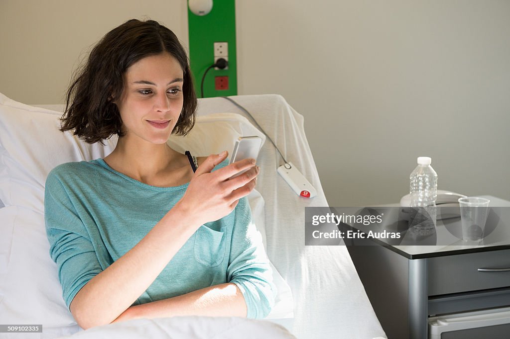 Female patient reclining on a hospital bed and text messaging