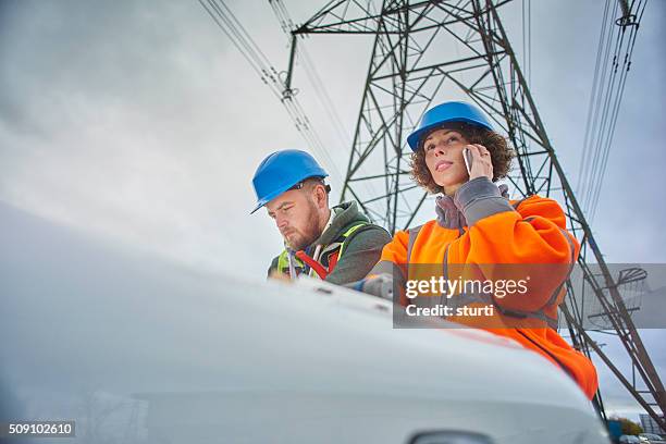 ingenieros bajo una torre de conducción eléctrica - all people fotografías e imágenes de stock