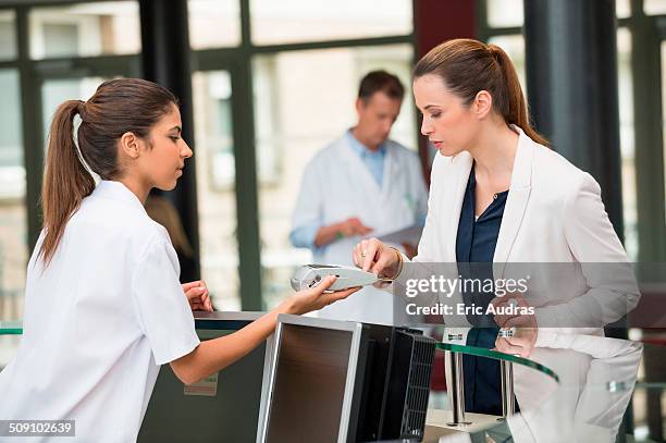 female doctor making payment with credit card at hospital reception desk - reception of france stock pictures, royalty-free photos & images
