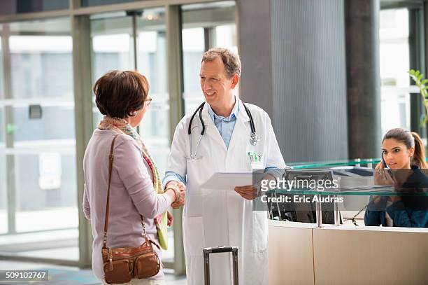 male doctor shaking hands with his patient at hospital reception desk - reception stock-fotos und bilder