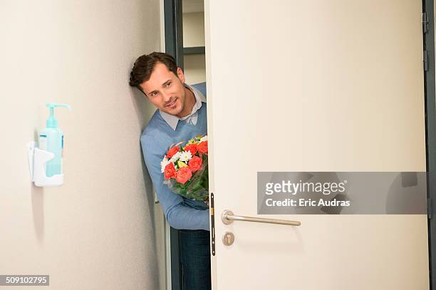 man peeking through an open door with a bouquet of flowers in hospital room - visit stock-fotos und bilder