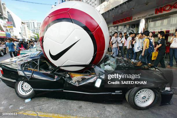 Thai shoppers look on at an advertisement for Nike at Euro 2004 showing a BMW sports sedan buckling under the weight of giant football, outside a...