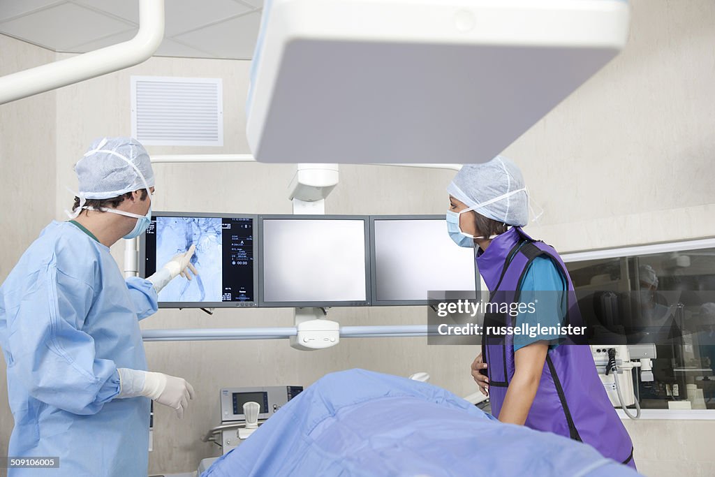Surgeon and nurse analysing MRI scan with patient in operating theatre