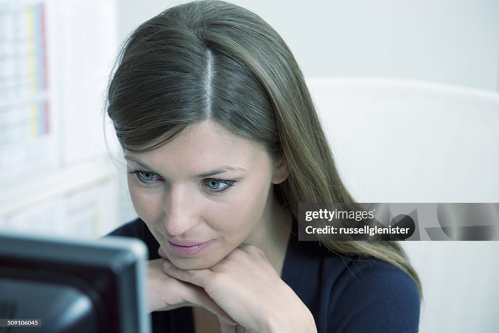 Portrait of woman working, looking at computer monitor in office