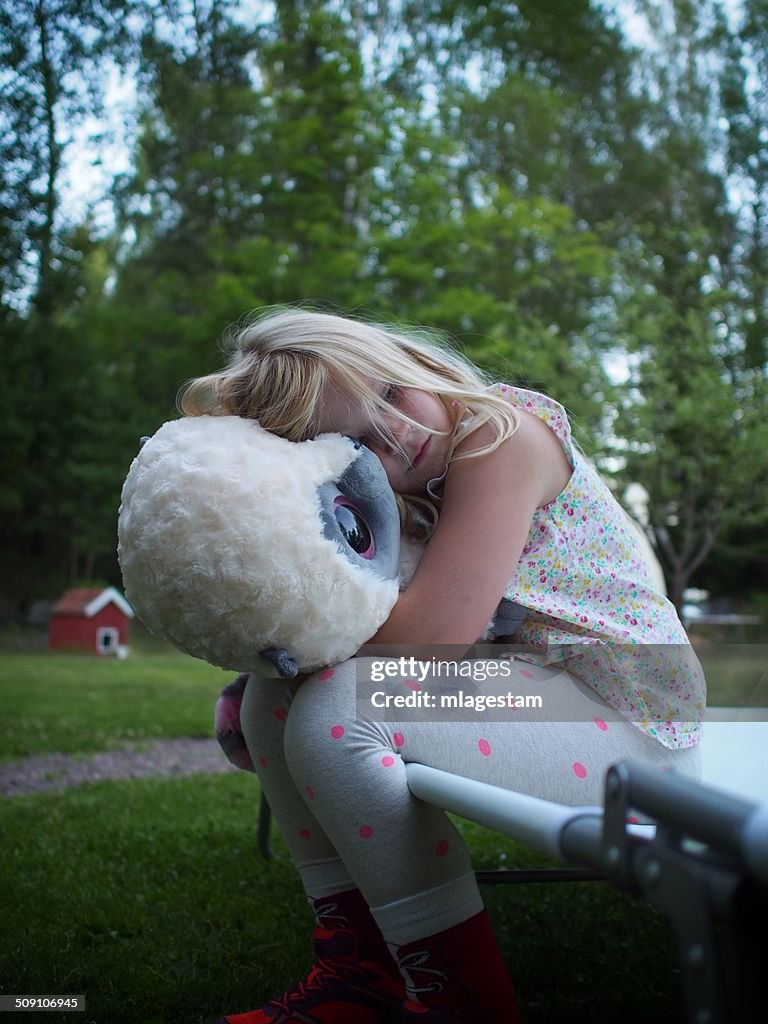 Sweden, Girl (6-7) hugging teddy bear in backyard