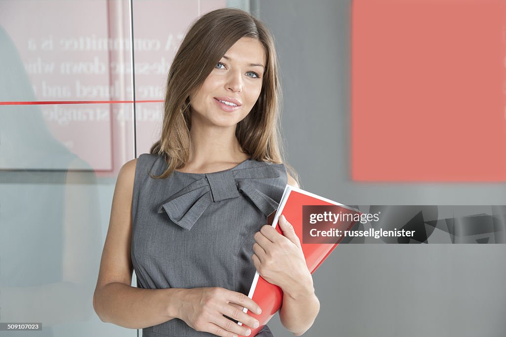 Portrait of a smiling businesswoman standing in office conference room holding a folder