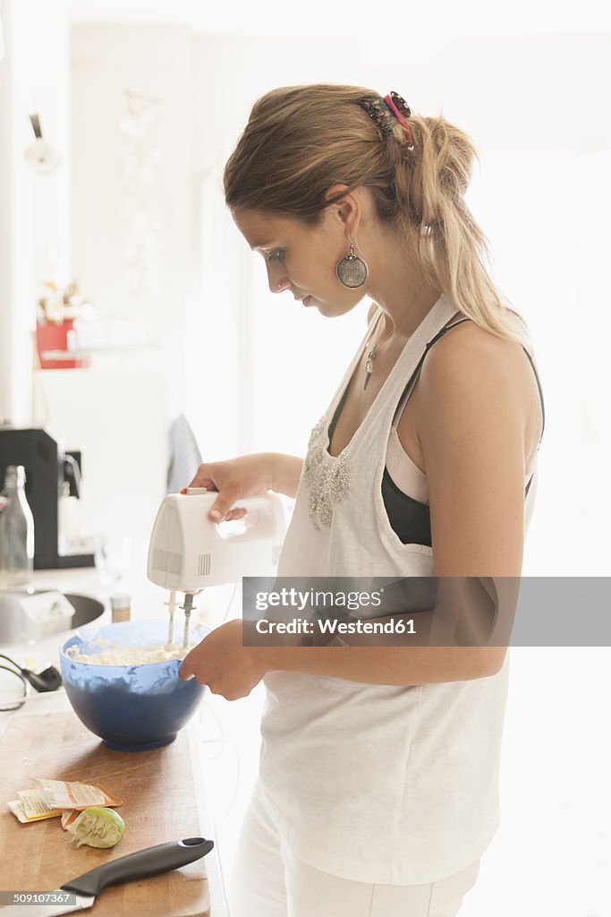 Young woman mixing dough at kitchen