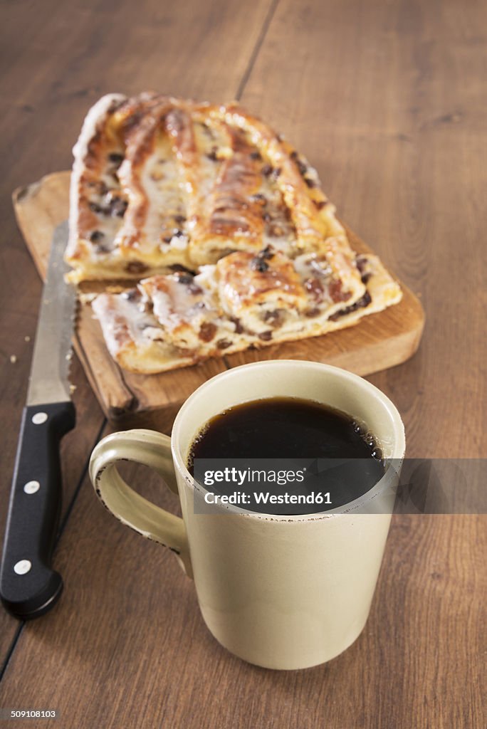 Cup of black coffee, knife and Danish pastry with marzipan on wooden board and table