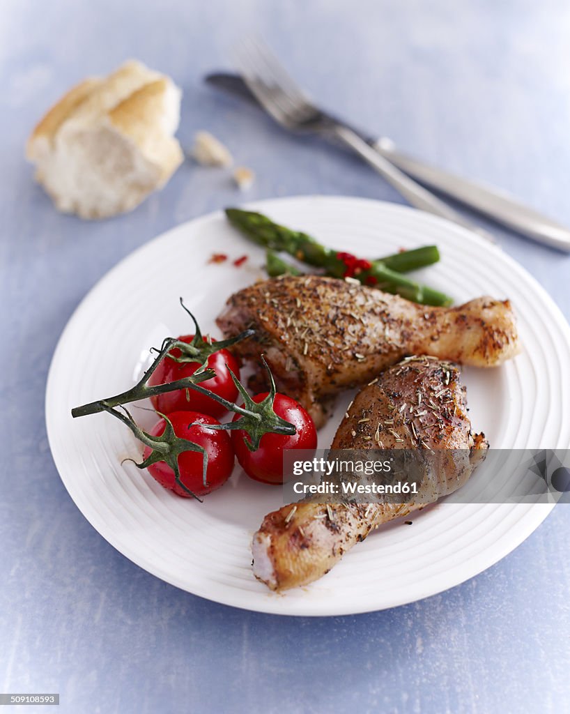 Chicken drumsticks on plate with tomatoes and asparagus