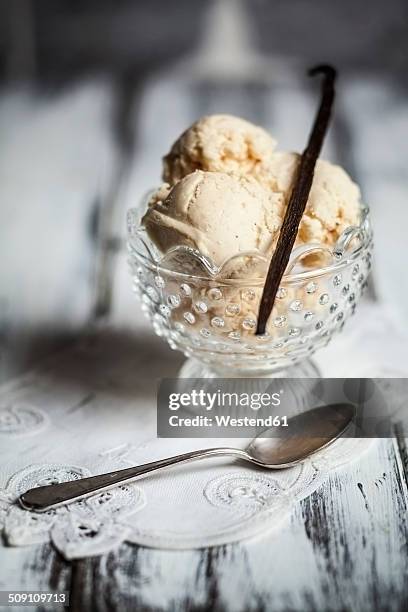 glass of vanilla ice cream with vanilla pod and spoon on wooden table - vanille stock-fotos und bilder