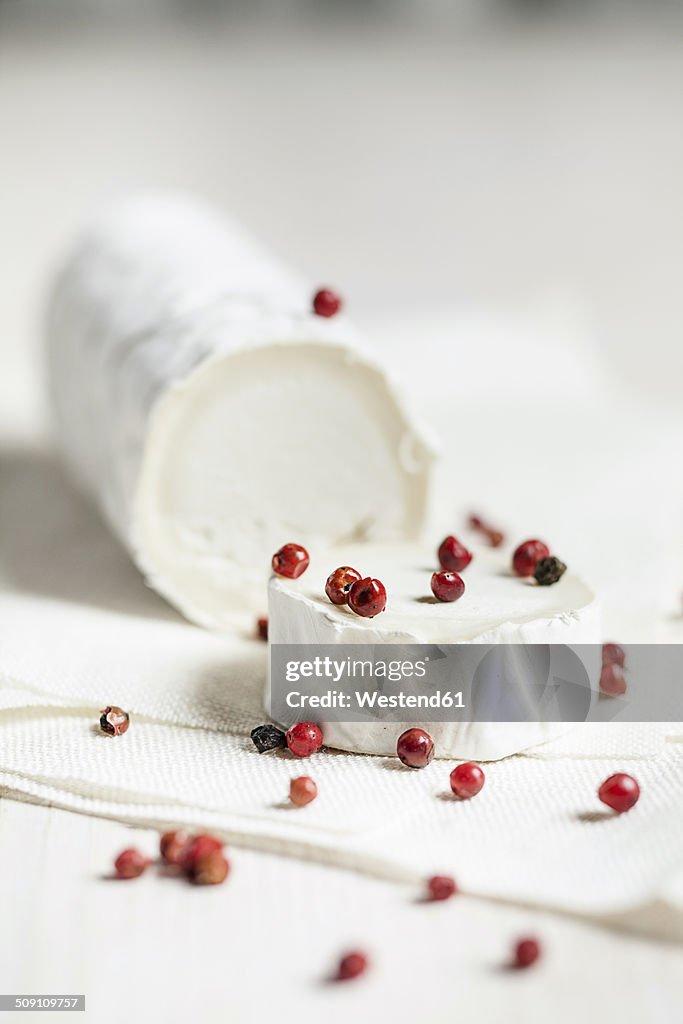 Roll of goat's cheese camembert with red peppercorns on white cloth