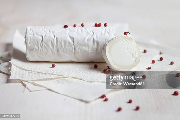 roll of goat's cheese camembert with red peppercorns on white cloth - queso de cabra fotografías e imágenes de stock