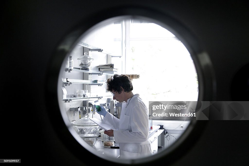 Female chemist working in lab watched through spy hole