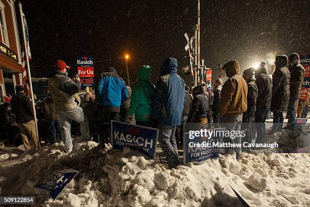 Supporters stand in the falling snow as Republican presidential candidate, Ohio Gov. John Kasich speaks at an election eve rally on February 8, 2016...