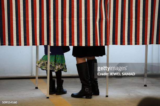 Woman is accompanied by a child inside a booth as she votes for the first US presidential primary at a fire station in Loudon, New Hampshire, on...