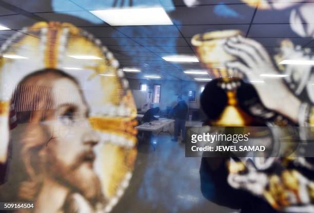 Local resident is reflected on a religious picture as he votes for the first US presidential primary at a church in Concord, New Hampshire, on...