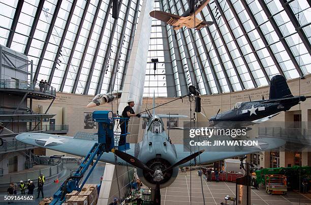 Lance Retallick, a technician with Weiss Theatrical Solutions secures a safety line as a World War II SBD Dauntless dive bomber is craned into...