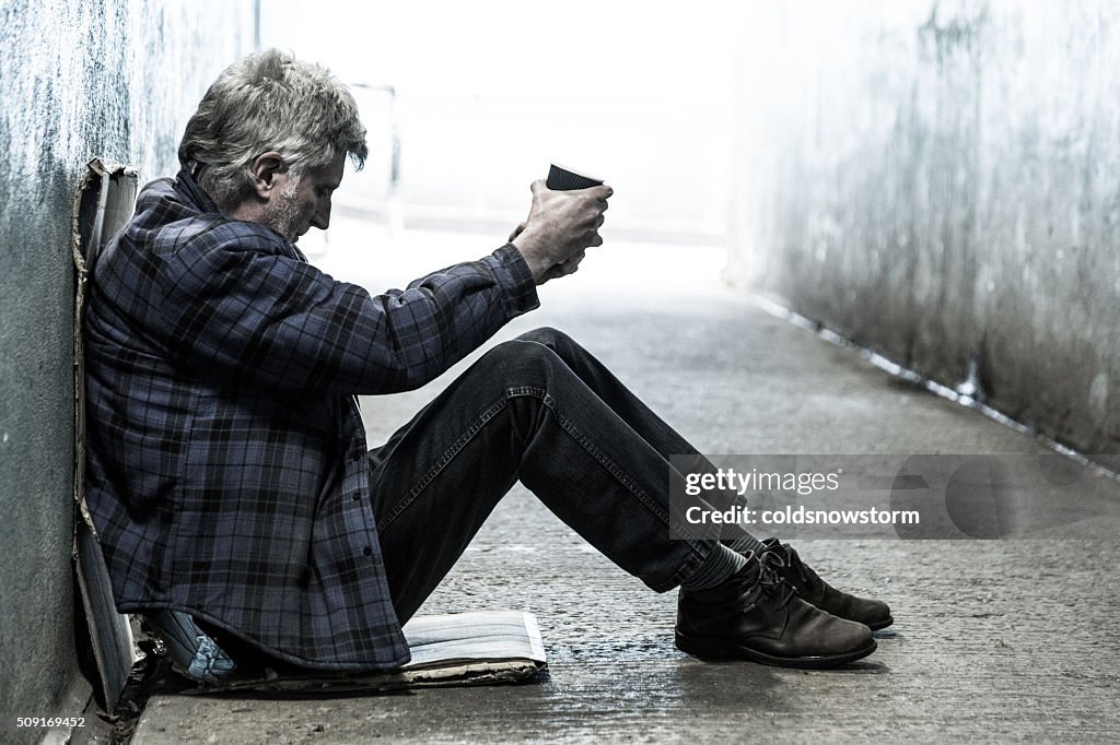 Homeless senior adult man sitting and begging in subway tunnel