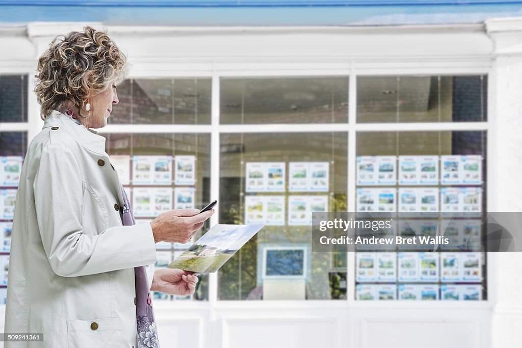 Senior woman outside estate agency uses mobile