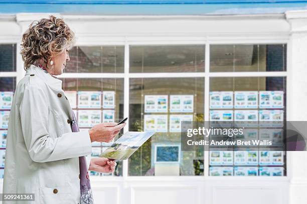 senior woman outside estate agency uses mobile - window stock pictures, royalty-free photos & images