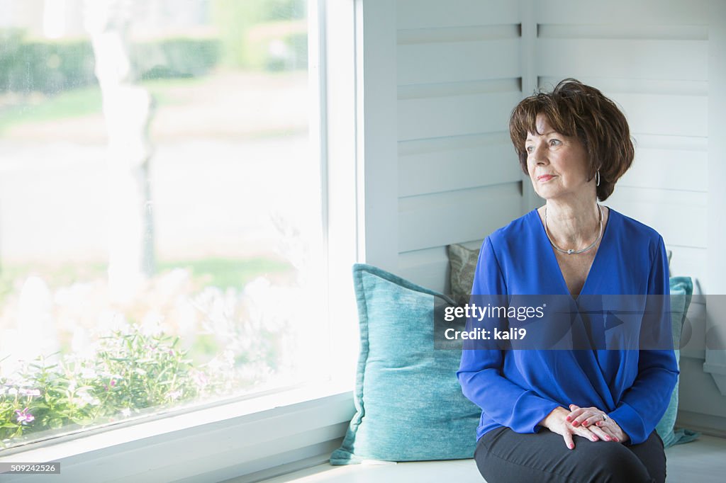 Senior woman looking out window with serious face