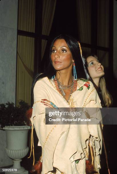 American actress and singer Cher wears beaded jewelry as she stands with arms folded in a Native American Poncho alongside her half-sister actress...