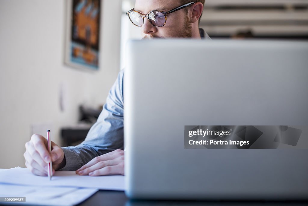 Businessman writing notes at laptop desk