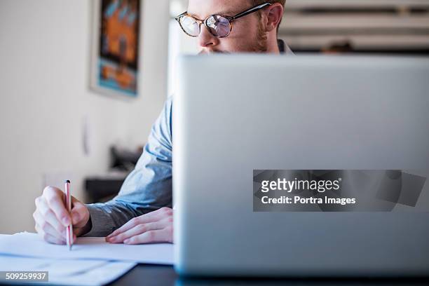 businessman writing notes at laptop desk - solo un uomo giovane foto e immagini stock