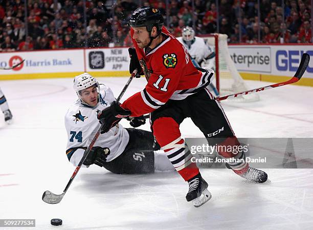 Andrew Desjardins of the Chicago Blackhawks turns to pass as Dylan DeMelo of the San Jose Sharks slips and hits the ice at the United Center on...