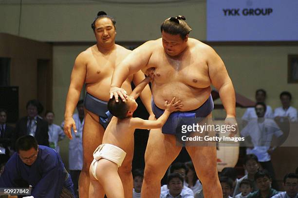 Sumo wrestler "fights" with a boy to the amusement of another wrestler in the back during a ceremony before a sumo tournament, on June 5, 2004 in...
